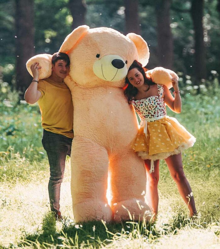 romantic couple together in forrest holding giant lifesize teddy bear in cream