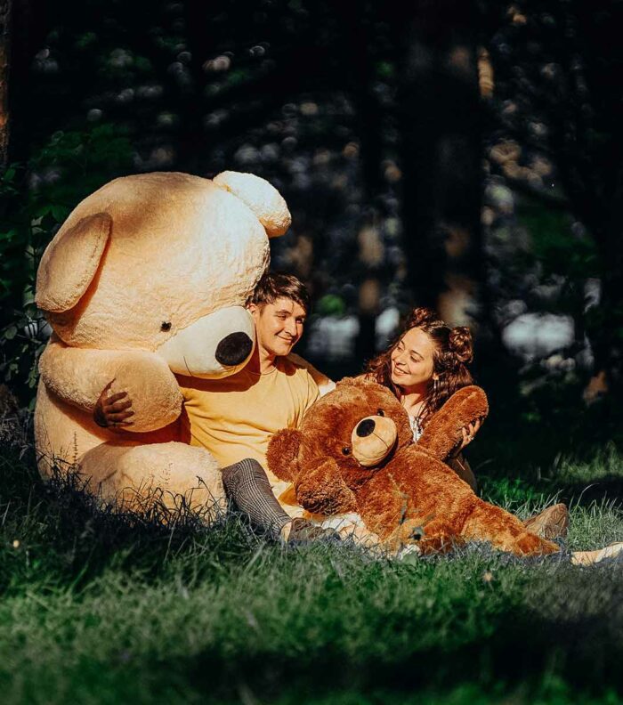 romantic couple together in forrest sitting with giant lifesize teddy bear in cream