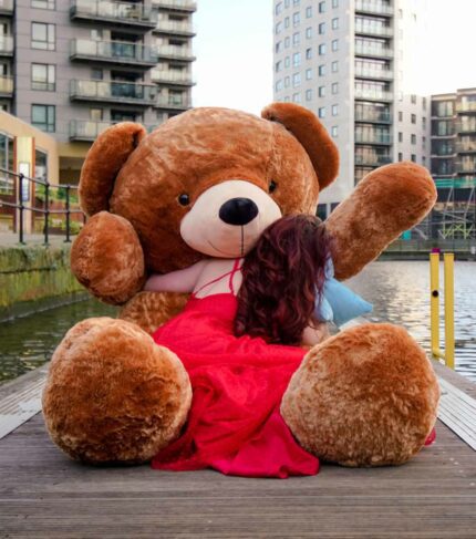 lady in red dress hugging giant teddy bear next to canal