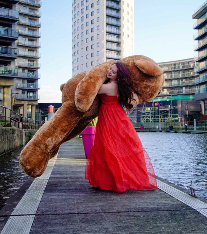 lady in red dress holding giant brown teddy bear