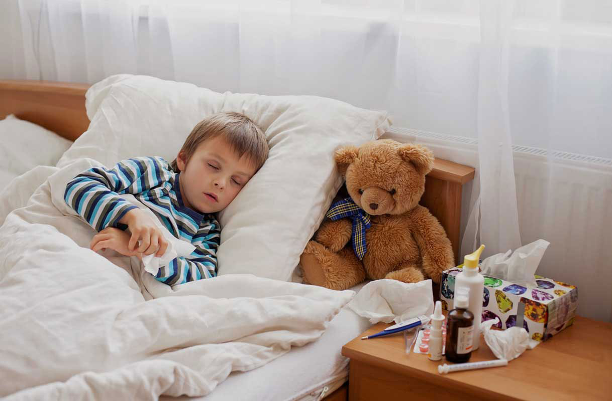 ill child in bed with teddy bear