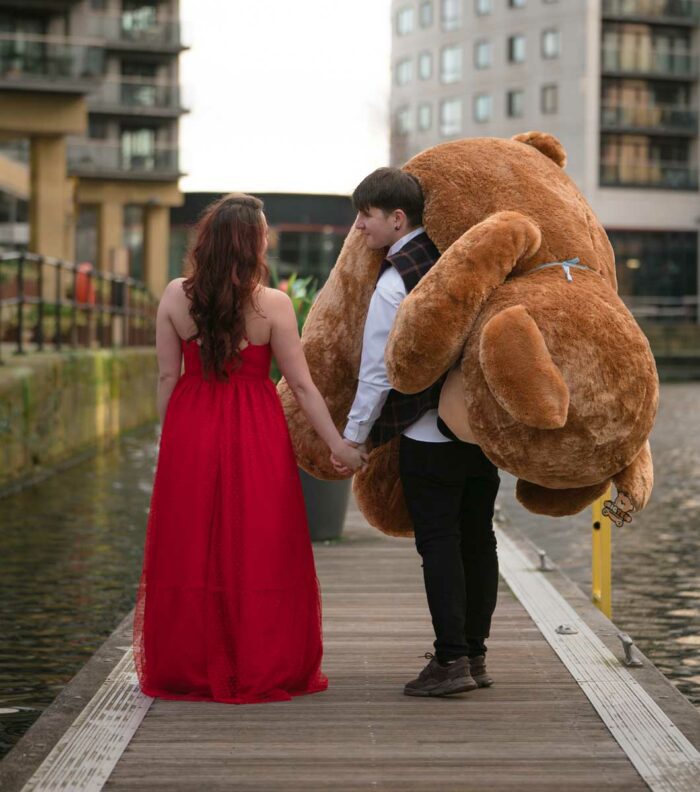 valentines couple holding hands in love with giant teddy bear gift