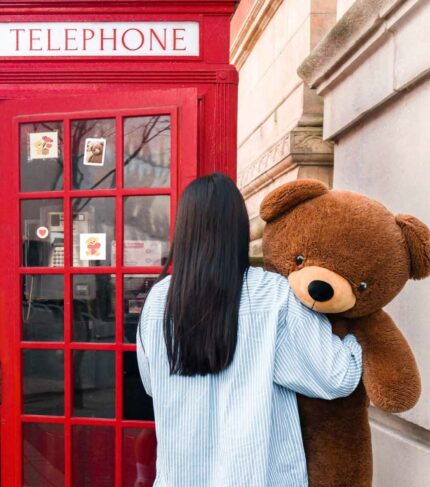 girl carrying teddy in London next to telephone booth