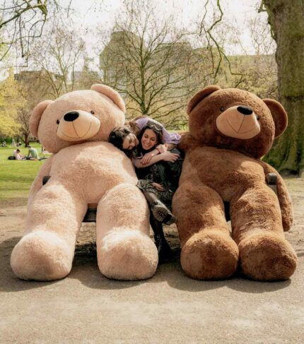 cute girls friends cuddling with giant brown teddy bears in park